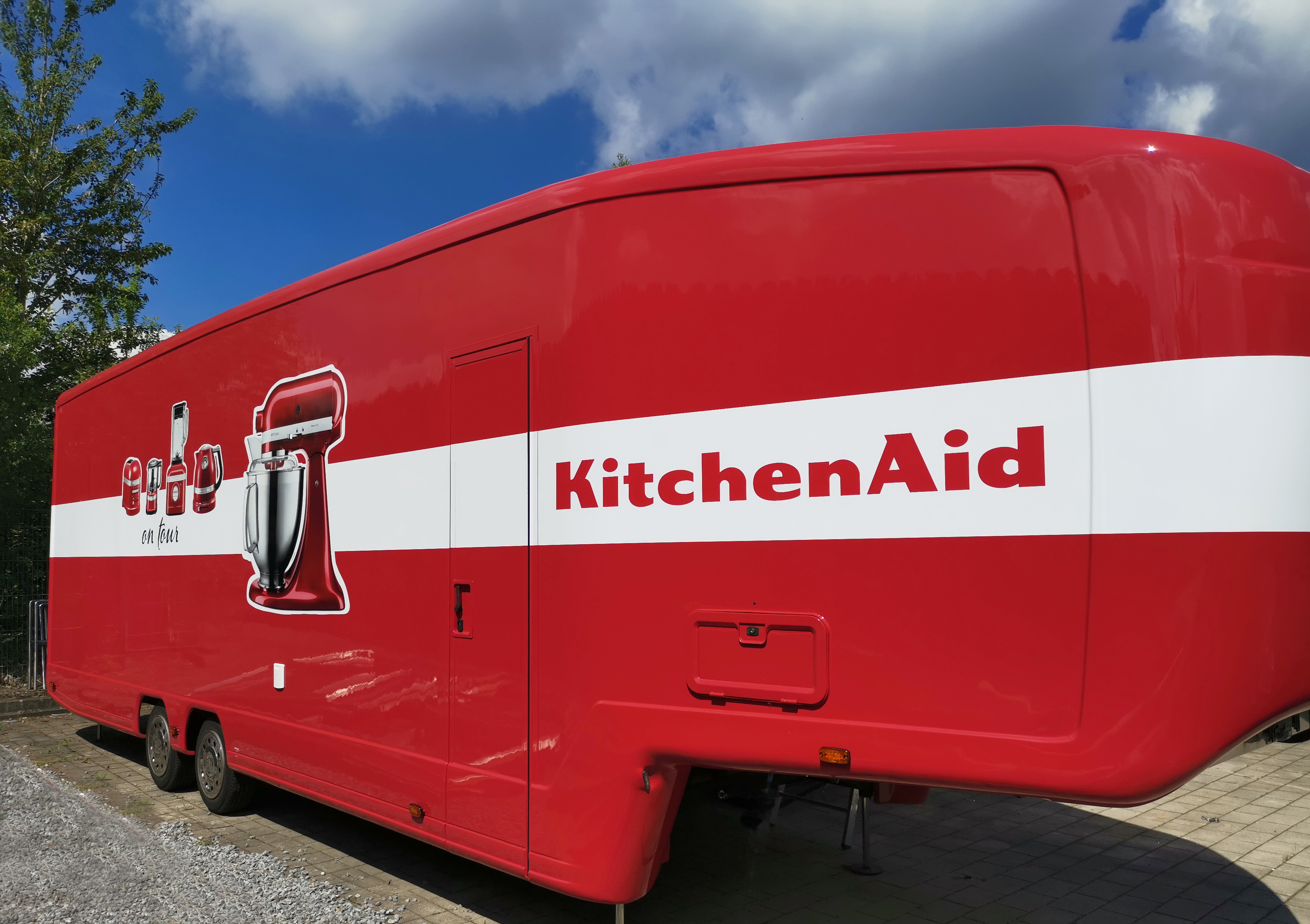 Roter KitchenAid-Sattelauflieger mit weißem Streifen, Logo und gemalten Küchengeräten gebrandet. 