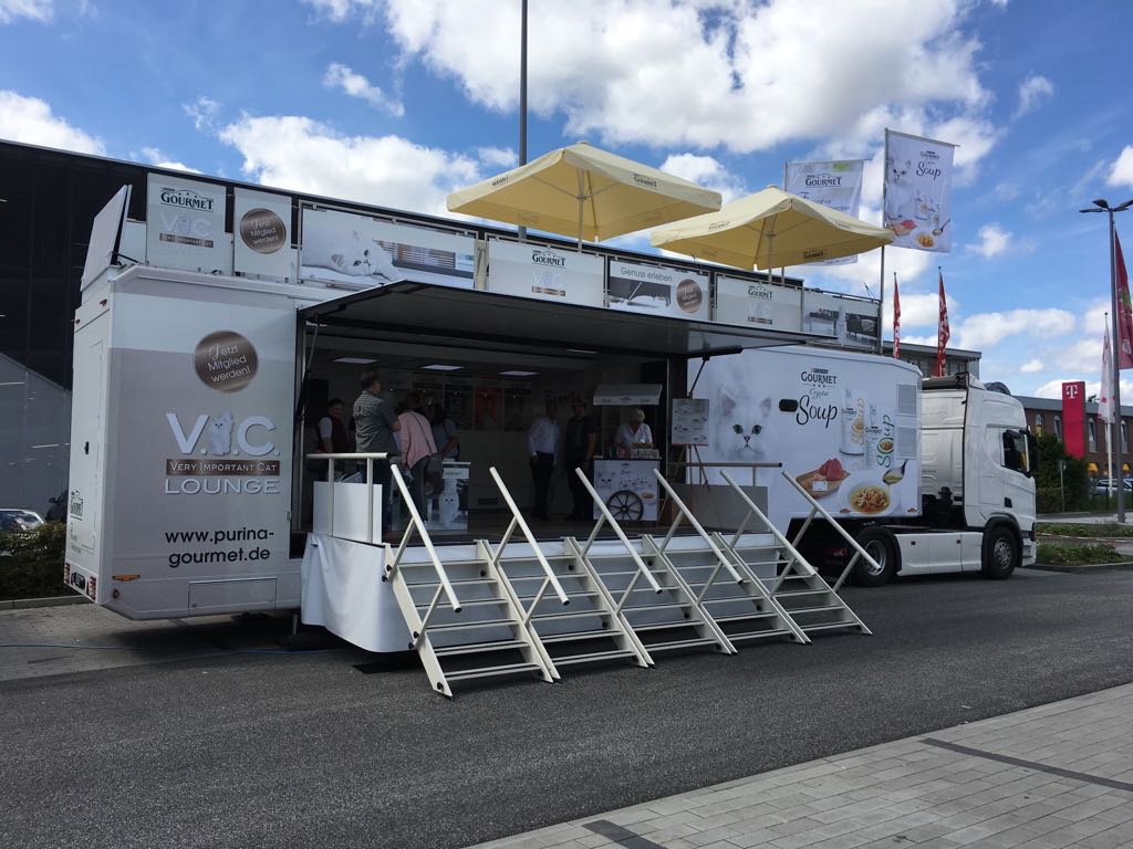 Weißer Sattelauflieger Showtruck mit geöffneter Seite und breiter Eingangstreppe.