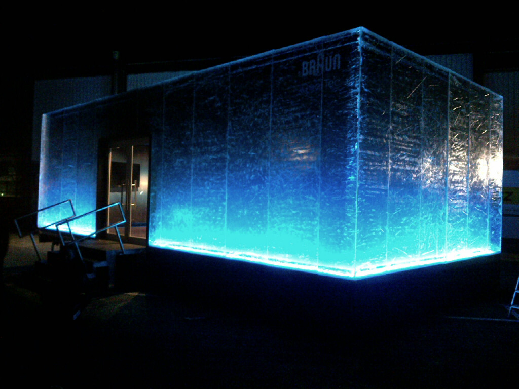 Ein rechteckiger, mobiler Raum leuchtet blau und wirkt wie ein riesiger Eiswürfel.