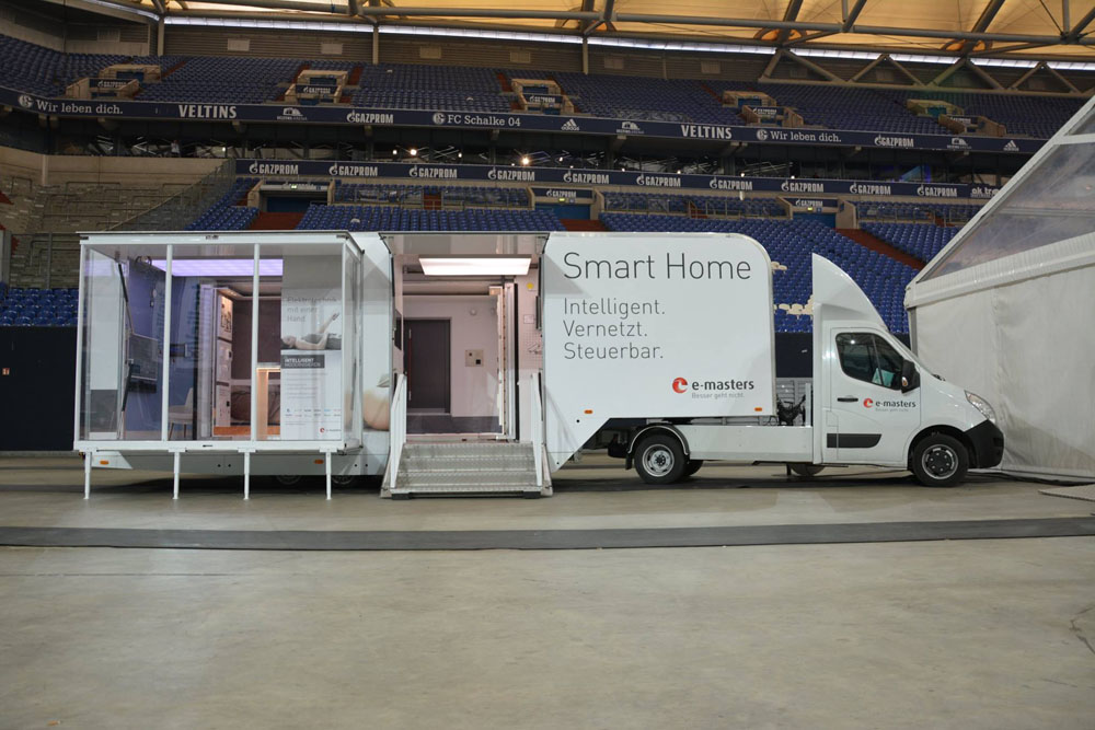Geparkter Ausstellungs-Truck mit begehbarem Mini-Sattelauflieger und verglaster Raumerweiterung steht in einem Stadium geparkt.