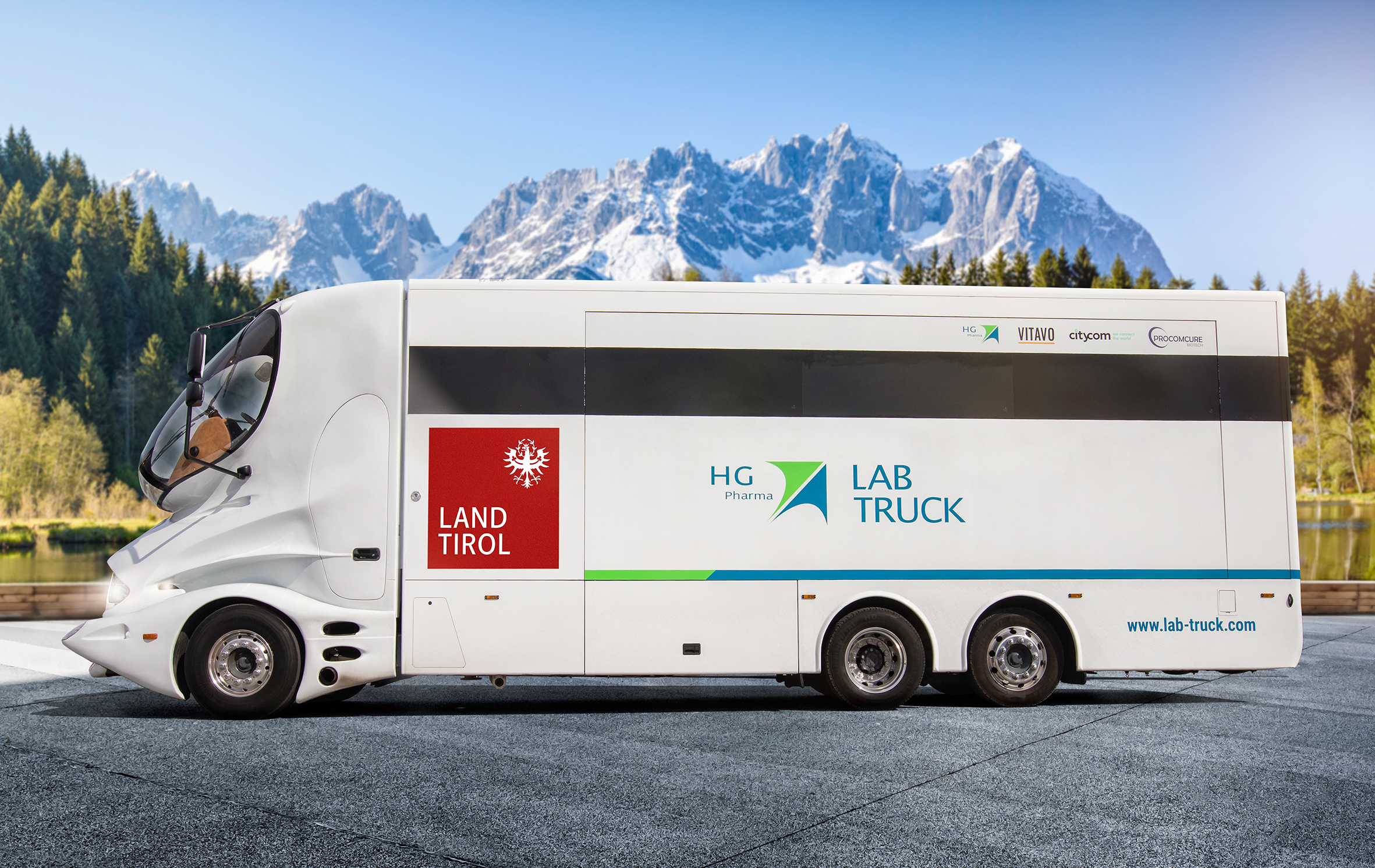 Weißer HG Pharma Lab-Truck mit Landtirol-Logo vor verschneiten Alpenbergen und Seen.