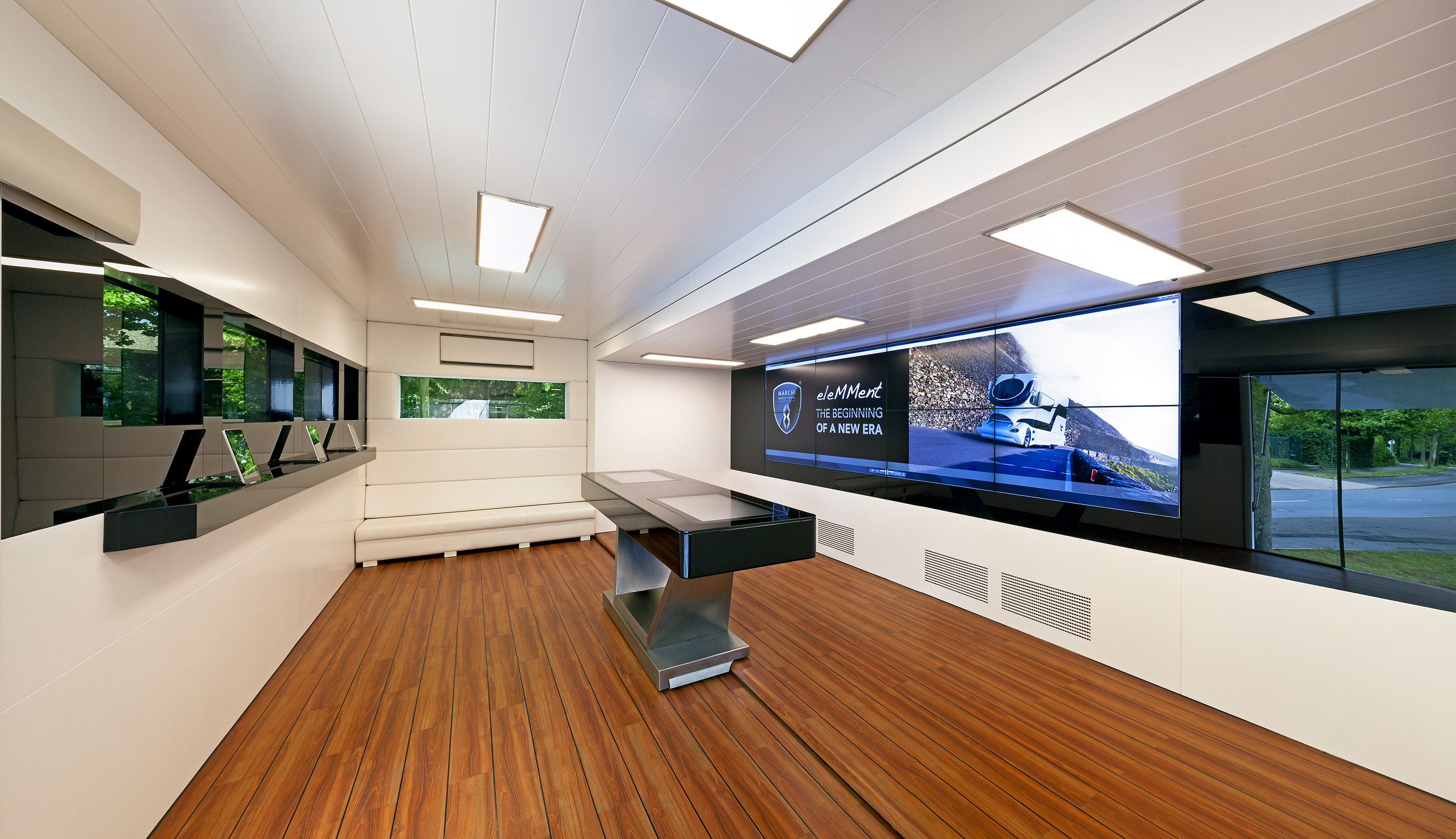 Moderner Design-Truck Innenraum mit Holzboden, hellen Wänden und großen Displays.