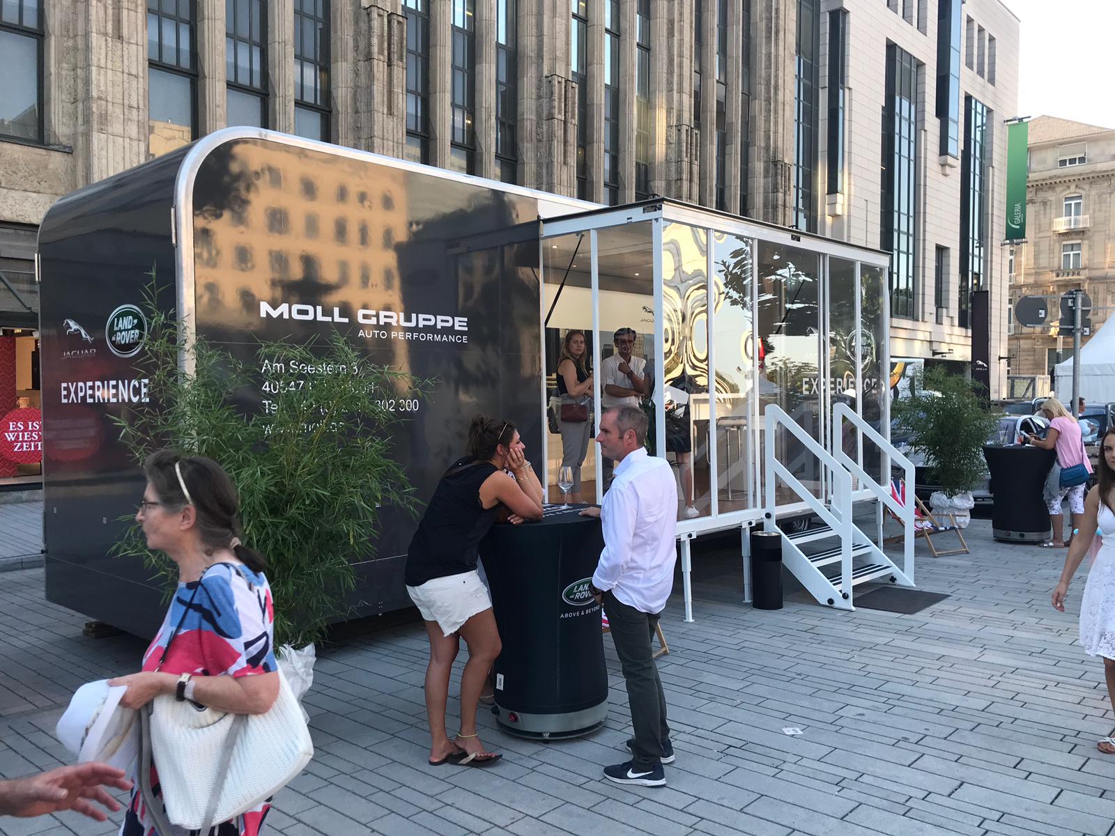 Marchi Lite Promotionanhänger von Moll Gruppe mit Besuchern auf Stadtplatz.