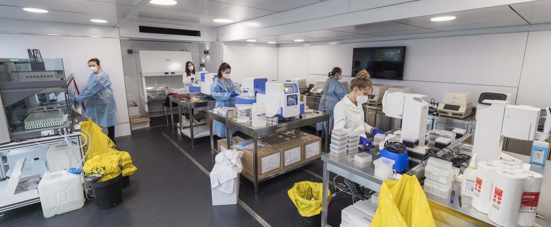 PCR Laborcontainer Innenraum: Laboranten in weißer Schutzkleidung arbeiten mit modernen Analysegeräten.