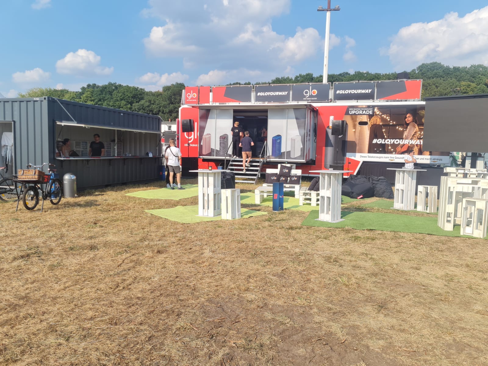 Rot-schwarzer Promotion-Sattelauflieger mit Besuchern auf sandigen Freiflächen mit Tischen. 