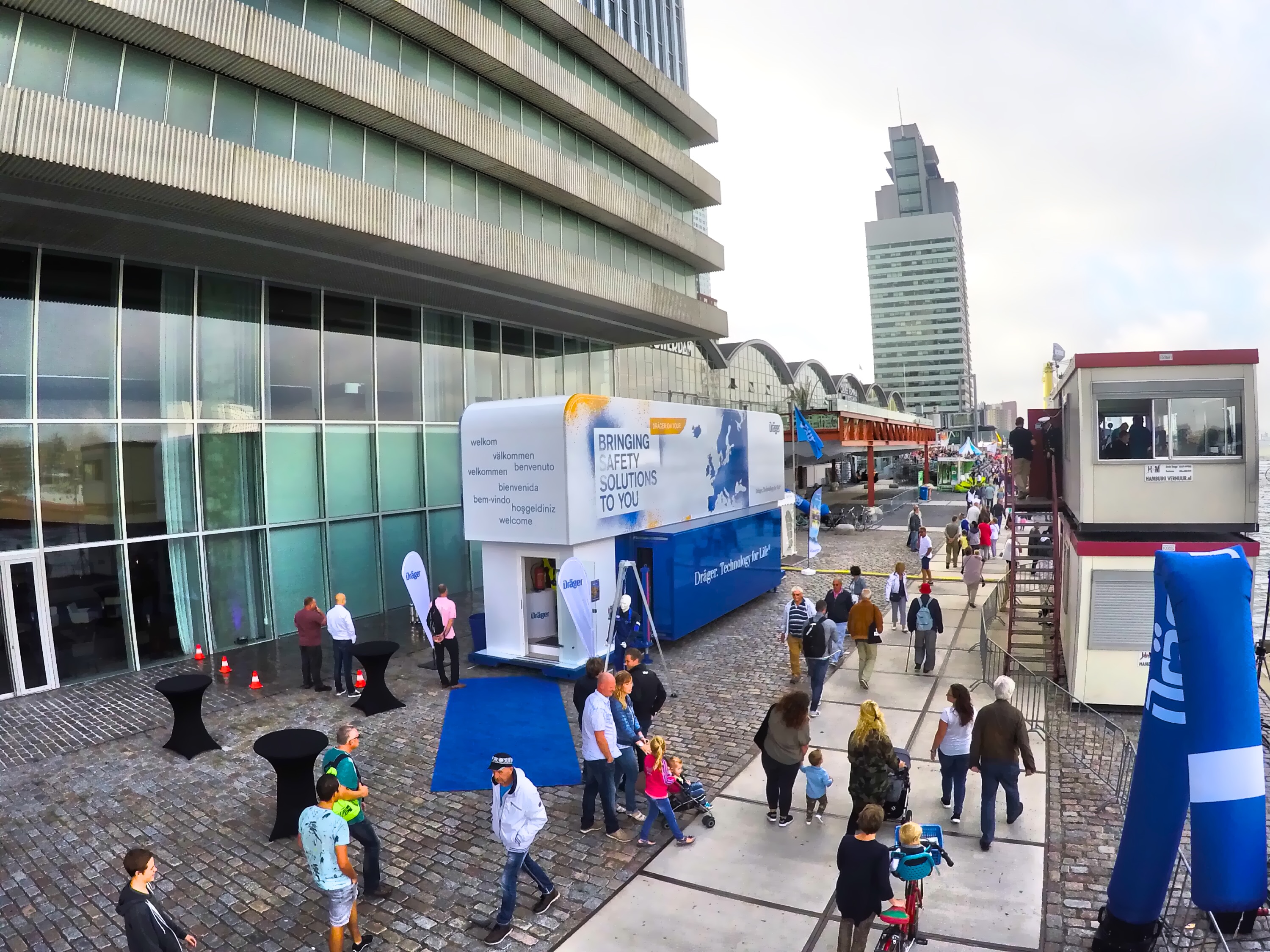 Showtruck zur Sicherheitskampagne mit vielen Besuchern auf urbanem Platz vor Hochhaus.