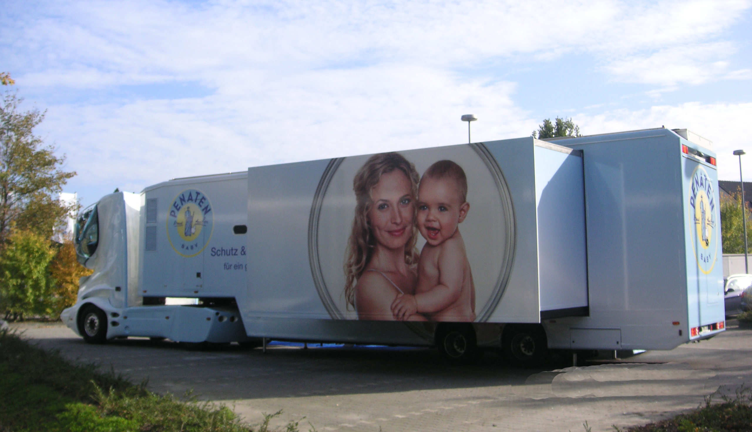 Penaten-Showtruck mit großem Sattelauflieger und ausgefahrener Raumerweiterung. Gebrandet mit Logo und Mutter-Baby-Bild.