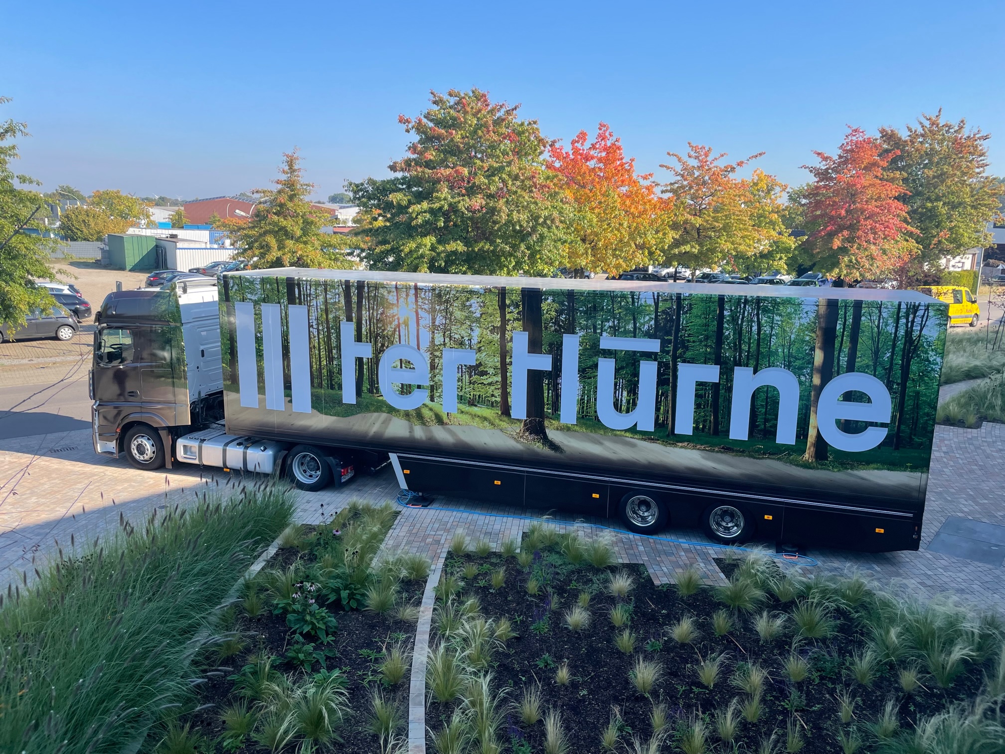 Sattelauflieger Truck mit großer "ter Hürne" Beschriftung parkt auf gepflastertem Platz, Herbstbäume im Hintergrund.