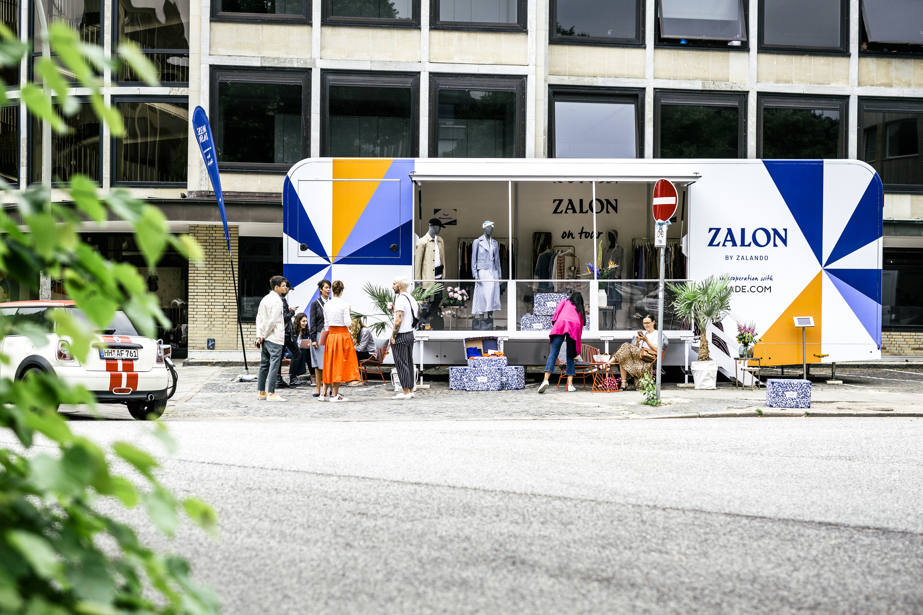 Begehbarer Marchi Lite PKW-Anhänger steht als Pop-Up-Store auf einem Stadtplatz. Großer verglaster Eingang erlaubt Blick auf Kleidung und Schmuck Warenauslage.