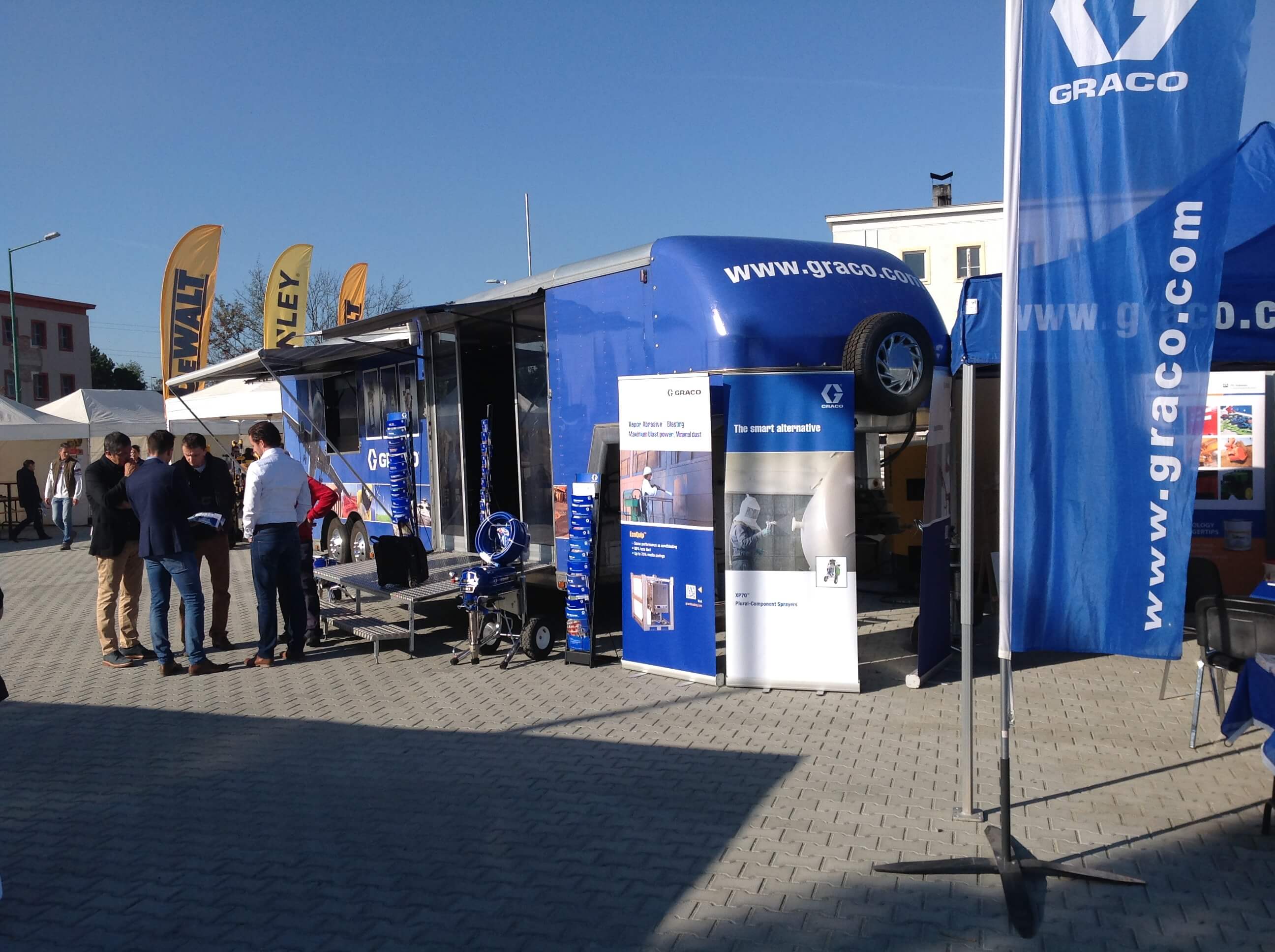 Graco Ausstellungsstand mit blauem Showtruck und Besuchern auf Messe.