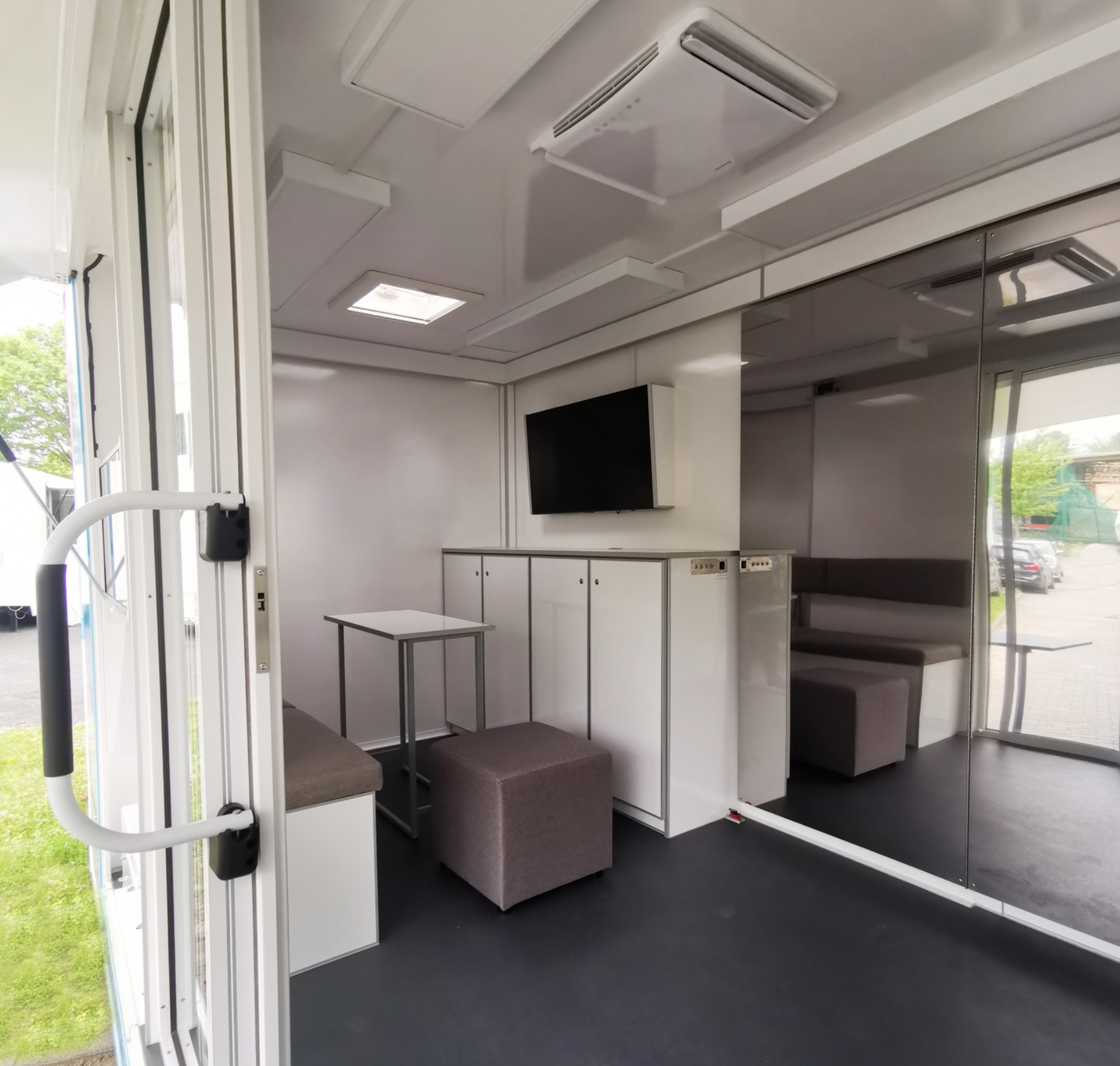 Moderner Innenraum eines Info Vans mit Sitzbereich, Fernseher und Schrankzeile.