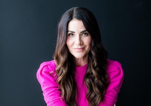 Tara Leigh-Cobble sitting on a chair in a pink sweater