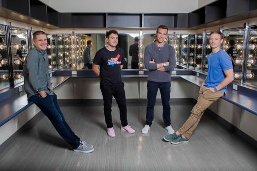Pod Save America hosts Jon Favreau, Jon Lovett, and Tommy Vietor standing in a dressing room alongside Dan Pfeiffer.