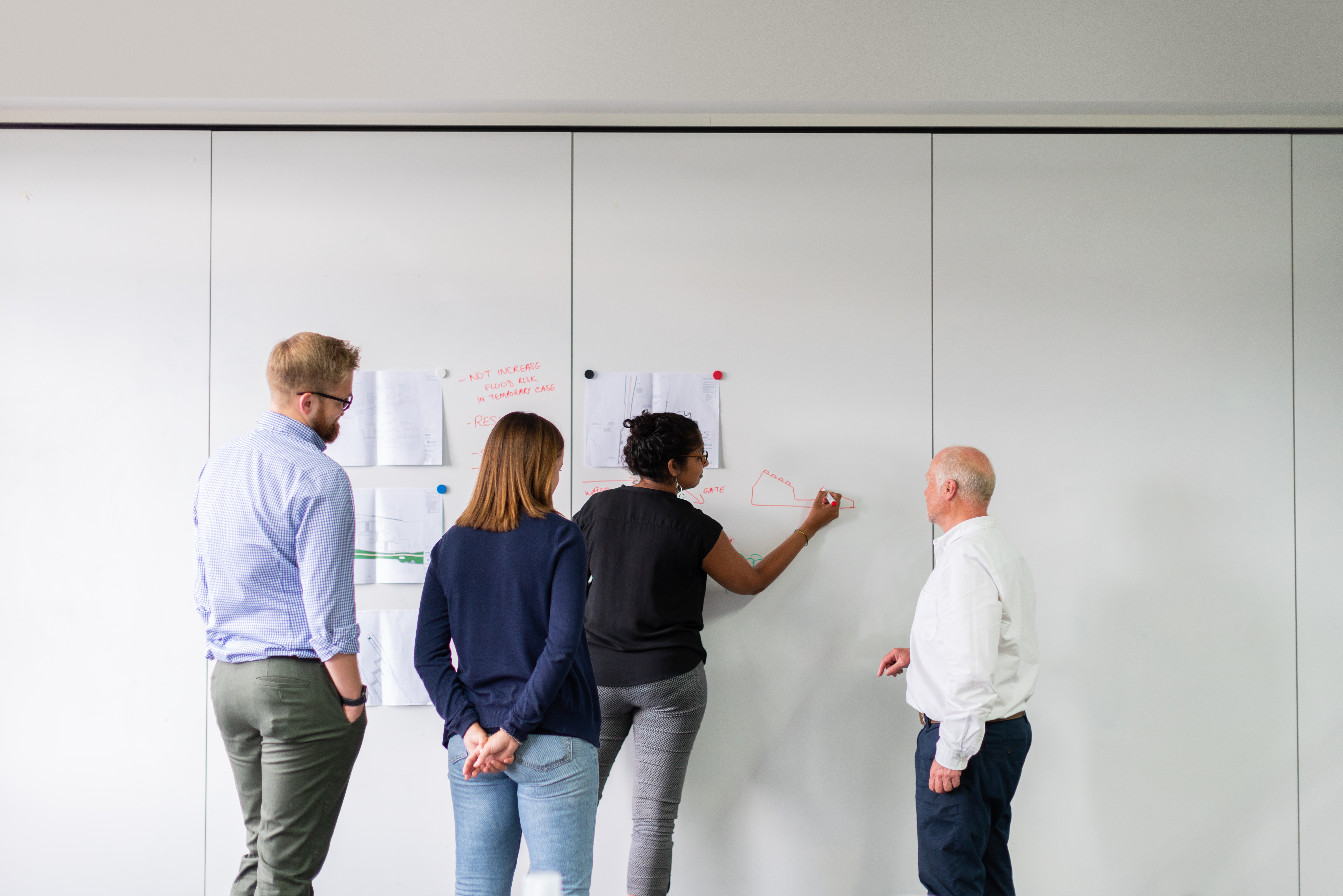 Four employees stand in front of a white board while one of them writes on it.