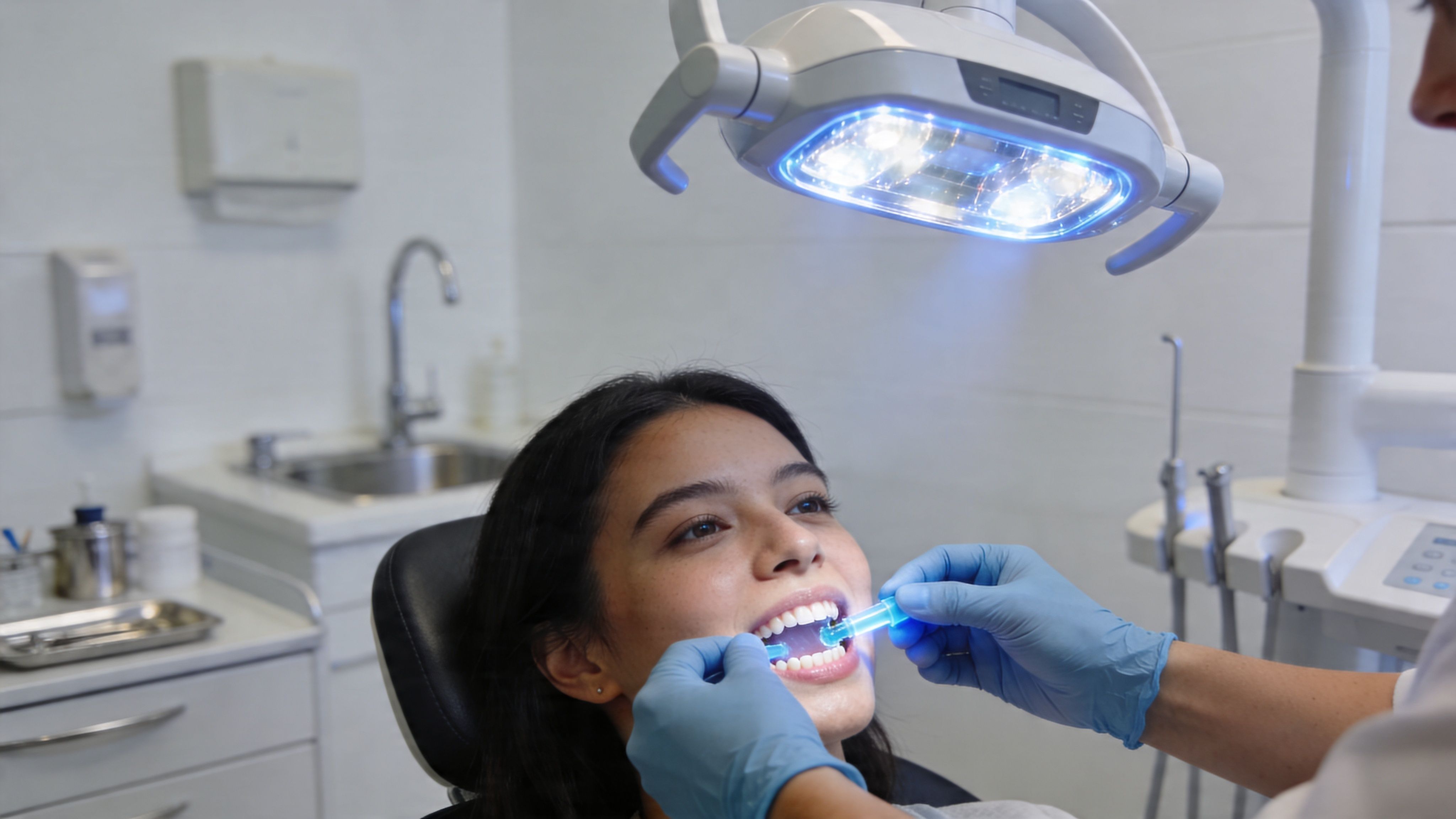 A professional dentist applying a blue teeth whitening light to a smiling patient in a modern clinic.