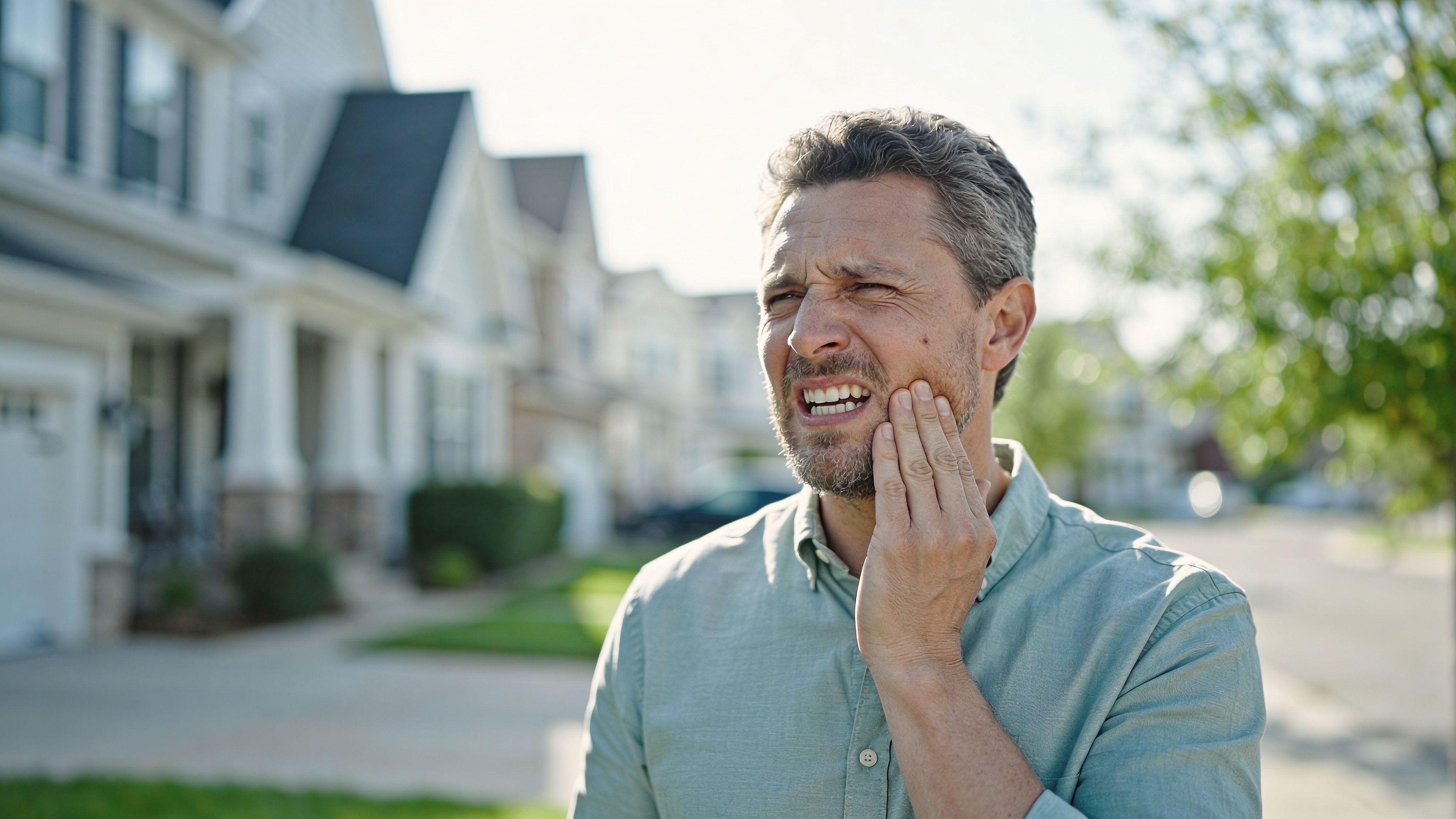 A middle-aged man suffering from acute toothache, touching his jaw with a pained expression outdoors.