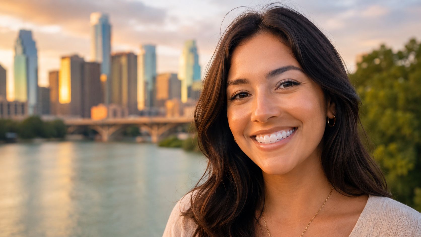 A smiling young woman with perfectly aligned teeth wearing clear aligners, outdoors with a city skyline.