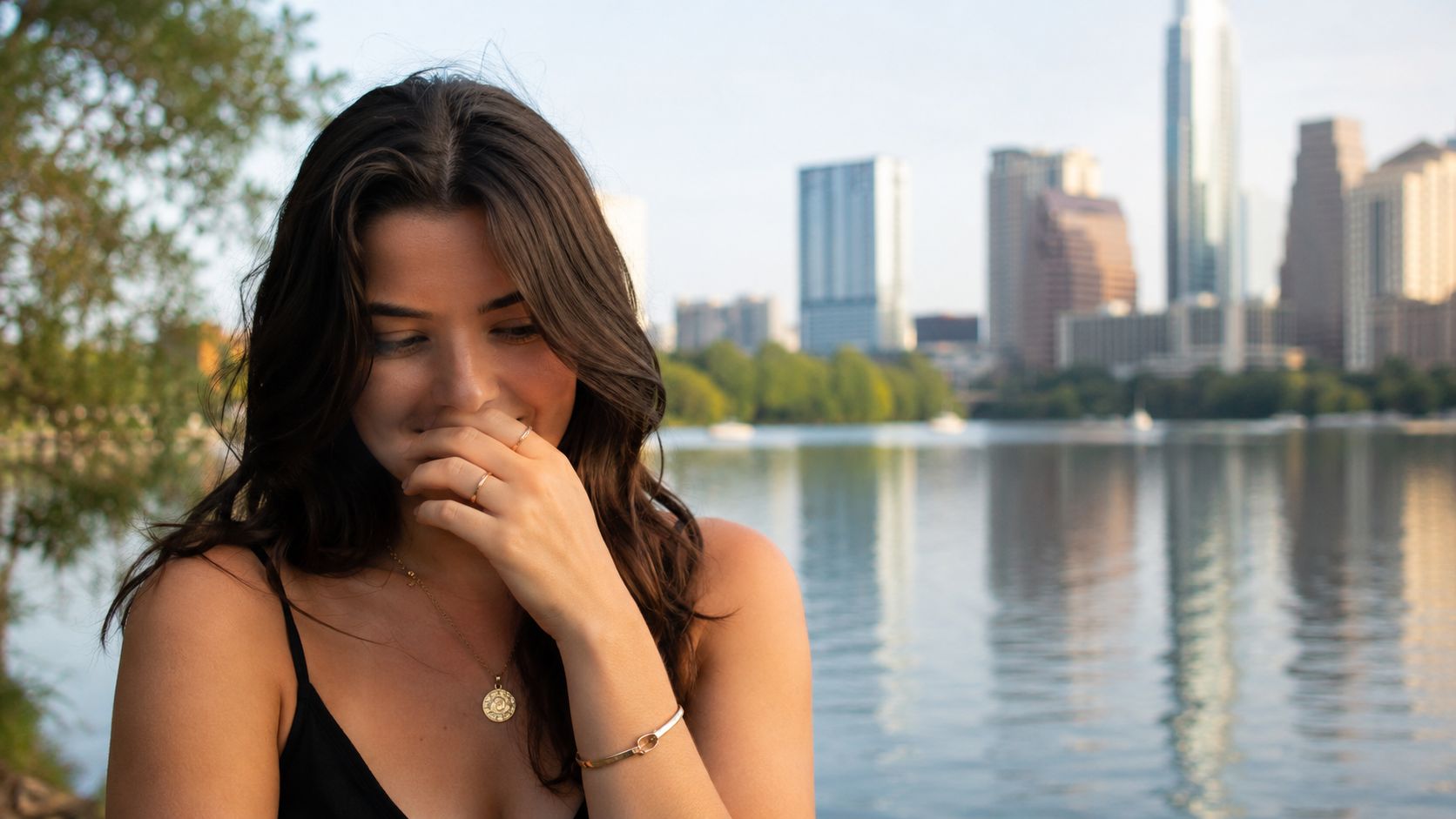 A happy young woman smiling shyly in front of the scenic Austin skyline and Lady Bird Lake.