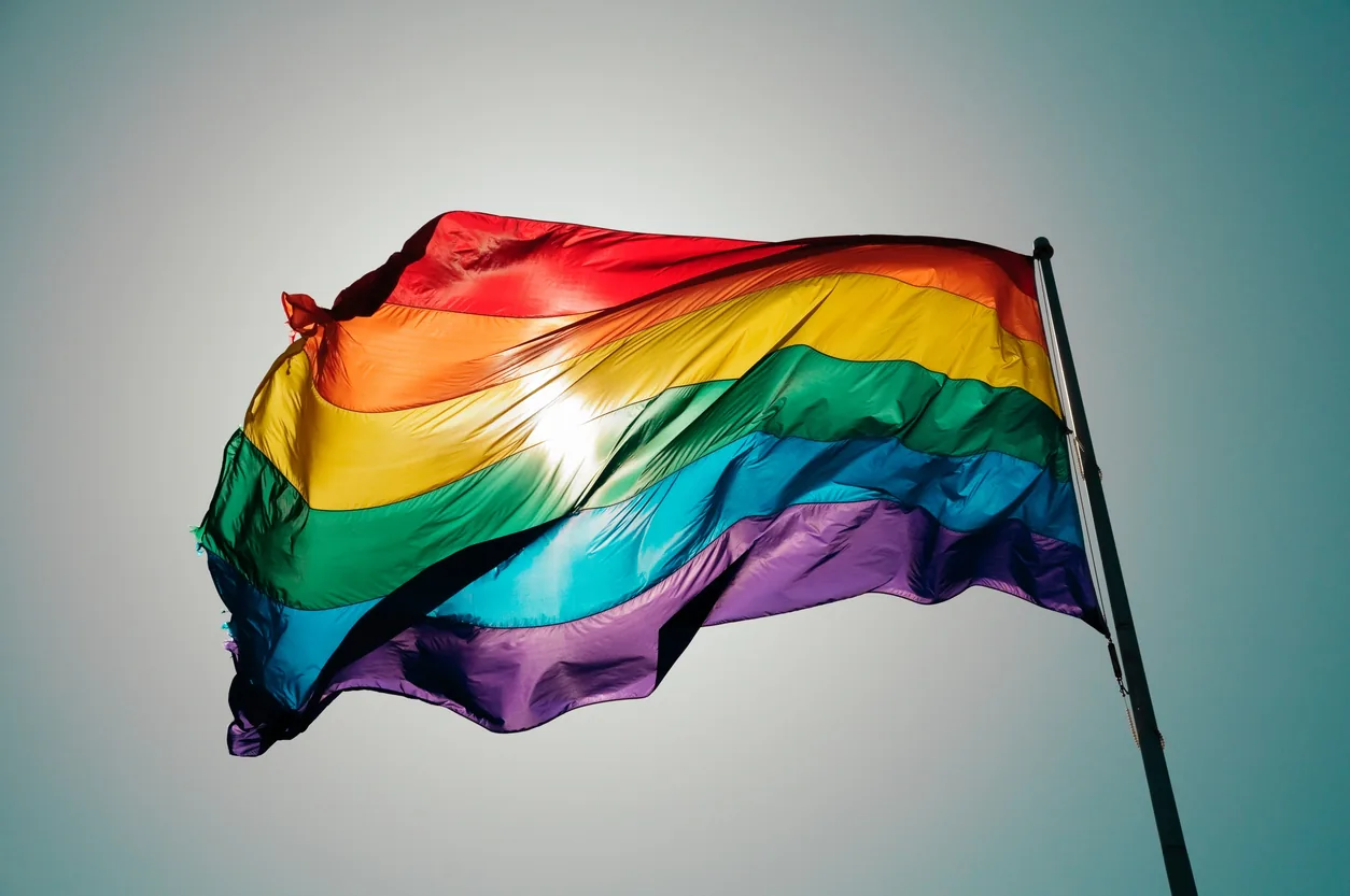 gay pride flag blowing in the sky against a blue sky