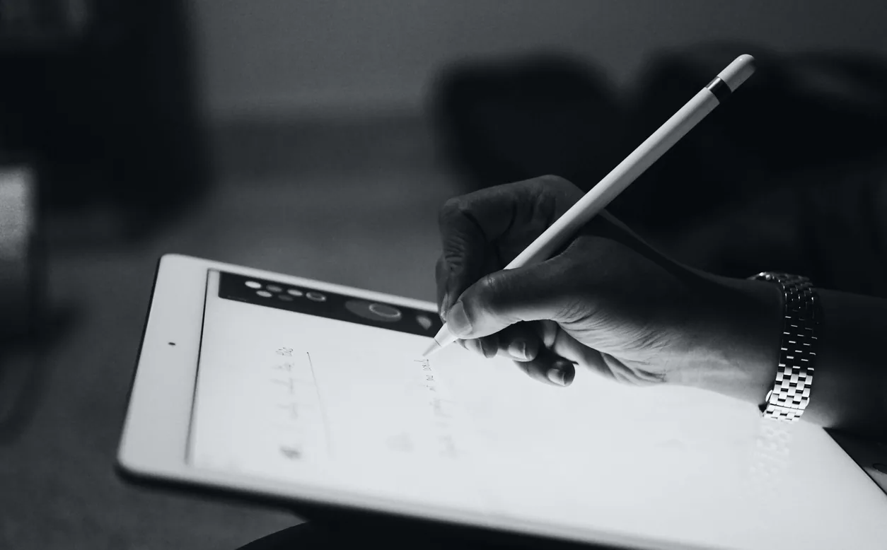 A hand writing notes with a stylus on a tablet