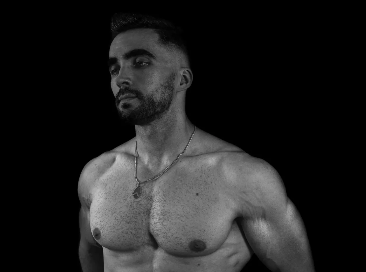 Head and chest of a bearded man against a black background showing light chest hair