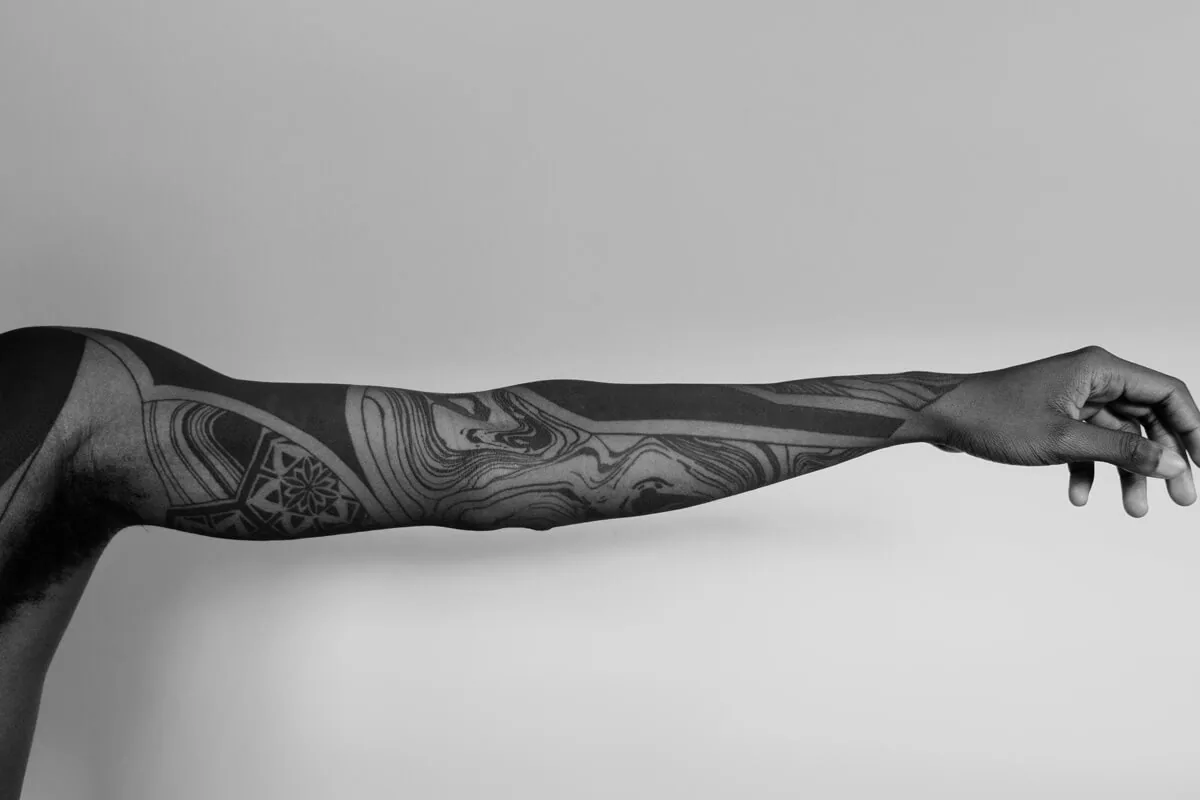 An outstretched arm with a full tattoo sleeve against a plain background