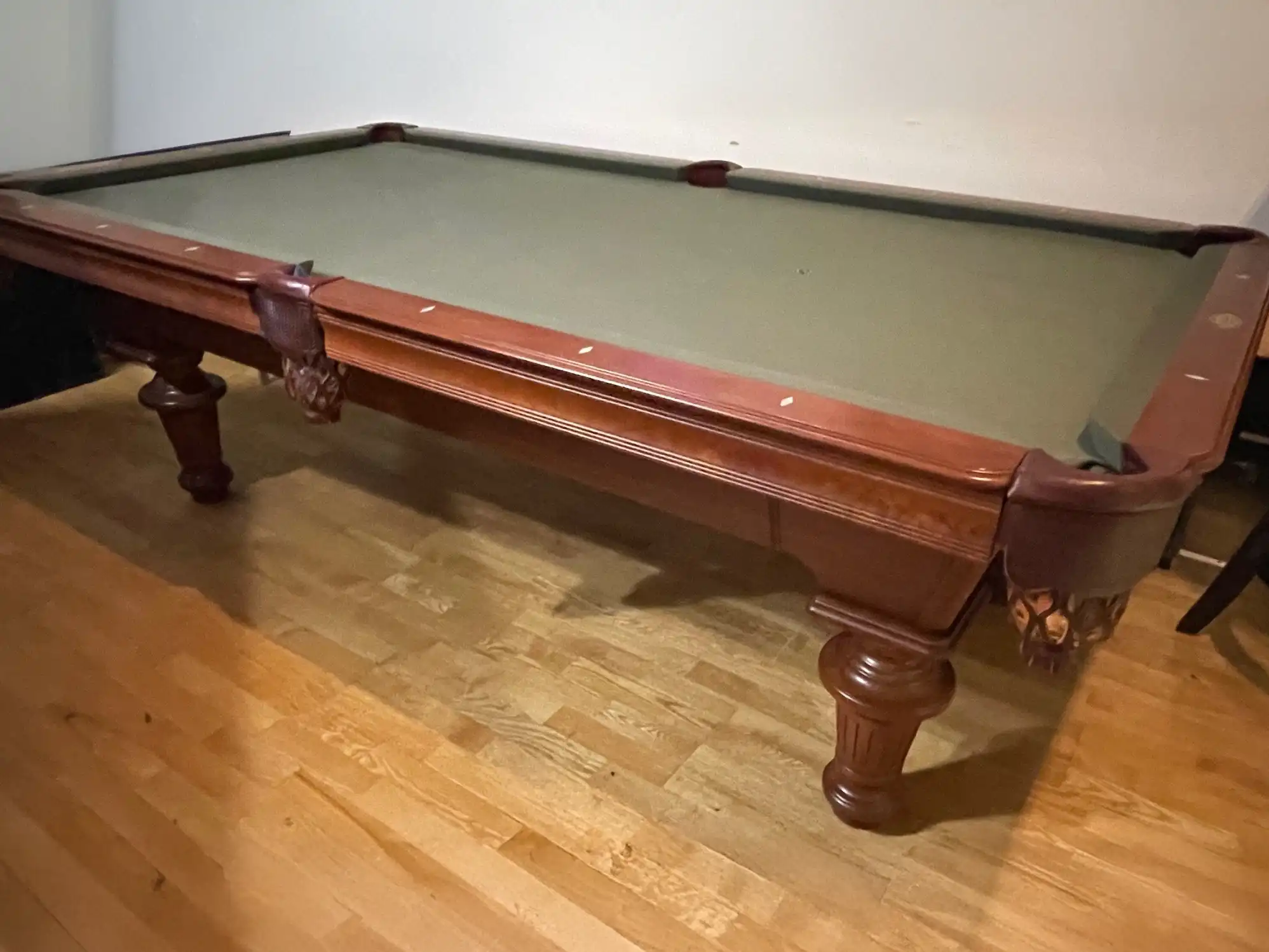  A pre-owned Olhausen Innsbruck pool table with a classic cherry finish and green felt, showcasing its carved legs and traditional design.