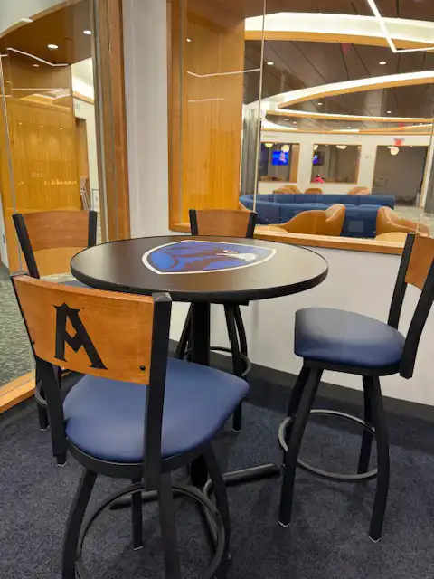 A game room at the University of New Haven with a round black and blue table and three chairs, all featuring the school's logo. 