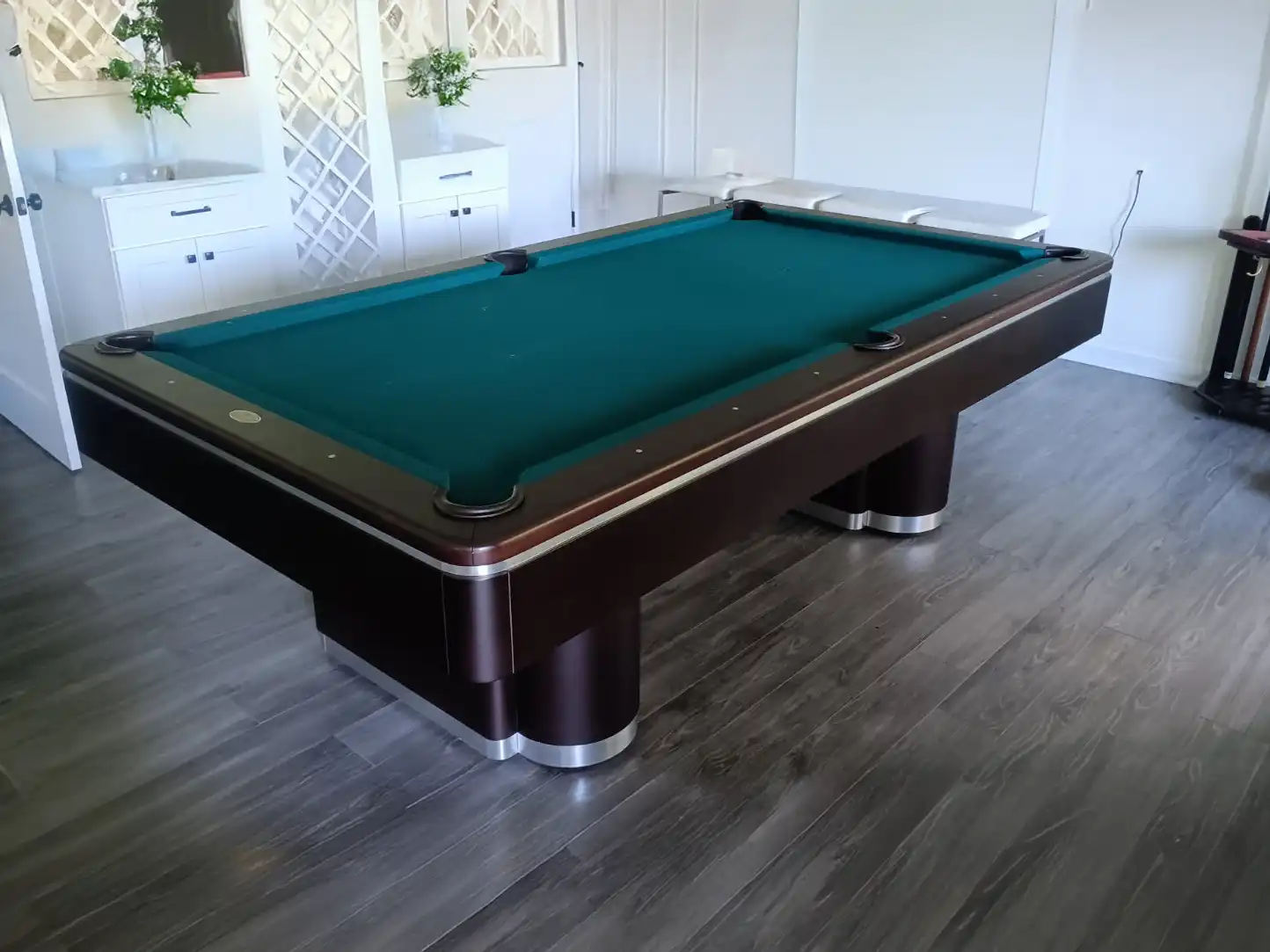 A sleek Olhausen Plaza pool table with a dark wood finish and a deep dark green felt surface sits on a gray wood-look floor.