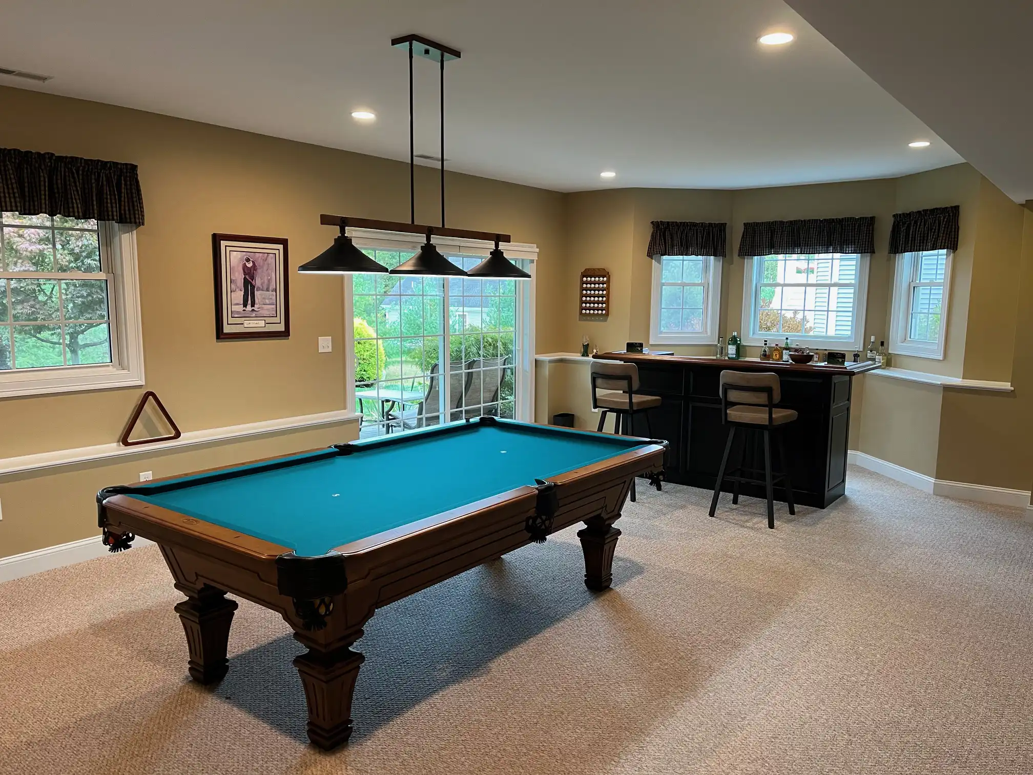 Basement game room featuring a teal, blue, or green pool table, modern hanging lights, a home bar with stools