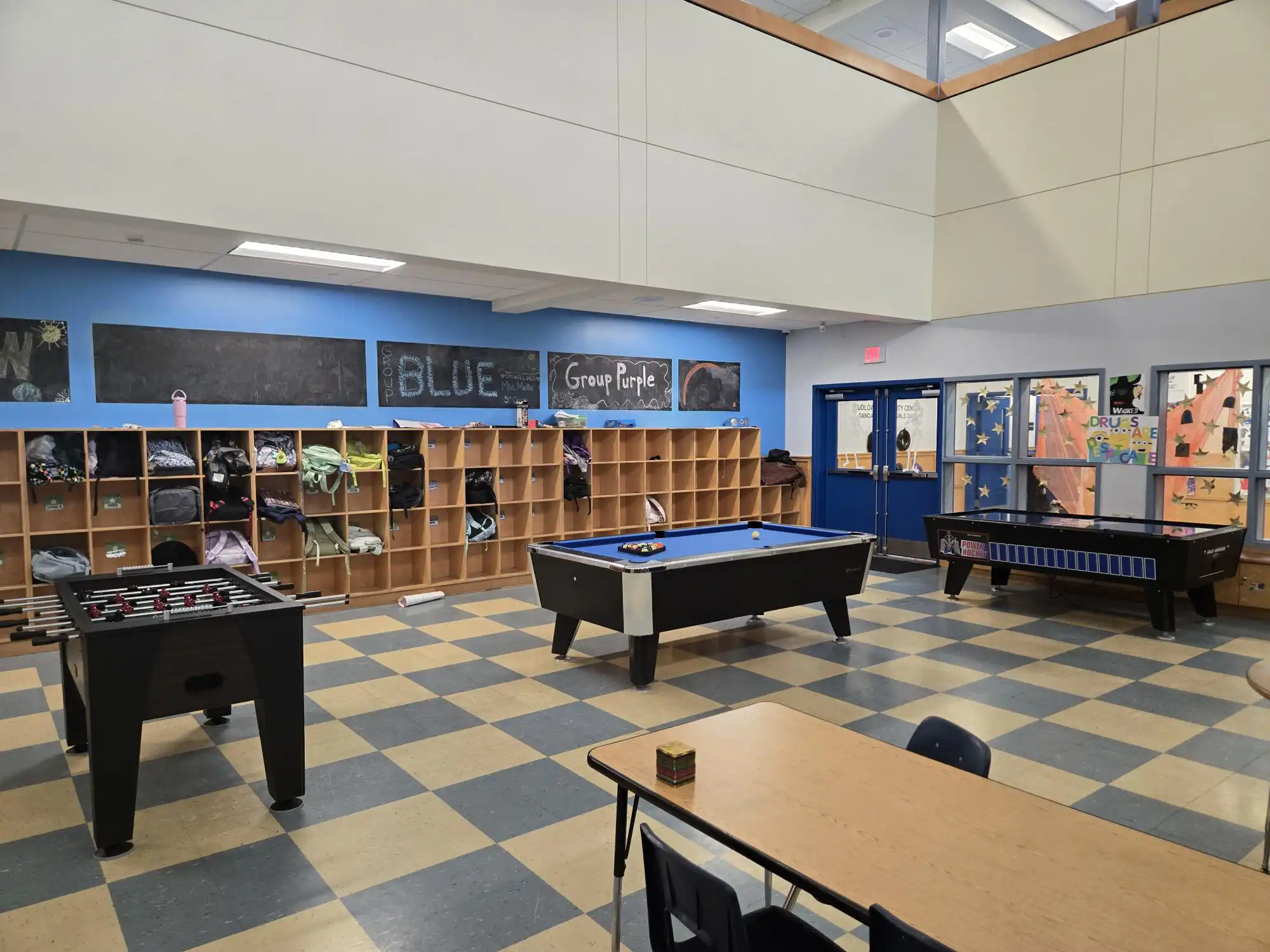 Game room at a Boys & Girls Club with a pool table, foosball, air hockey, and cubbies, featuring colorful decor and group signs on chalkboards.