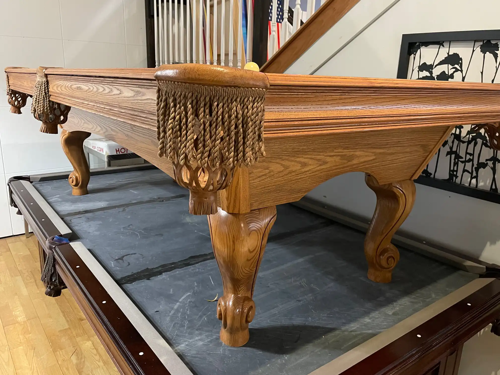 A Brunswick 8' Contender series pool table with wooden legs, ornate fringed pockets, and light oak wood grain finish in a basement game room.