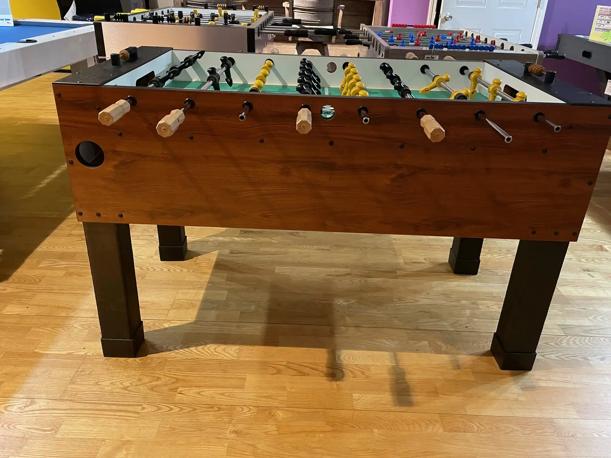 Tornado Twister foosball table with a wood grain cabinet, black legs, and yellow and black players displayed on a hardwood floor in a game room showroom.