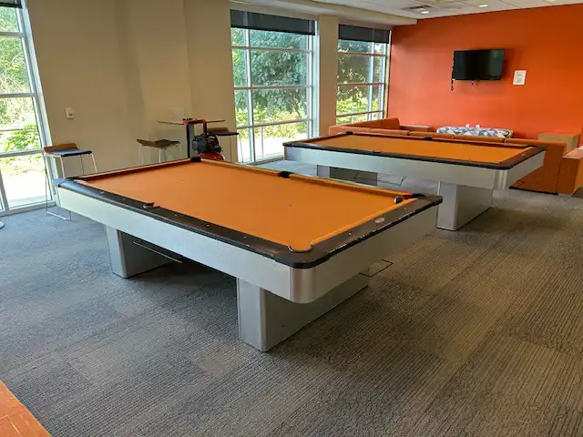 Two commercial pool tables featuring custom orange felt and grey laminate finish installed at the University of New Haven student lounge.