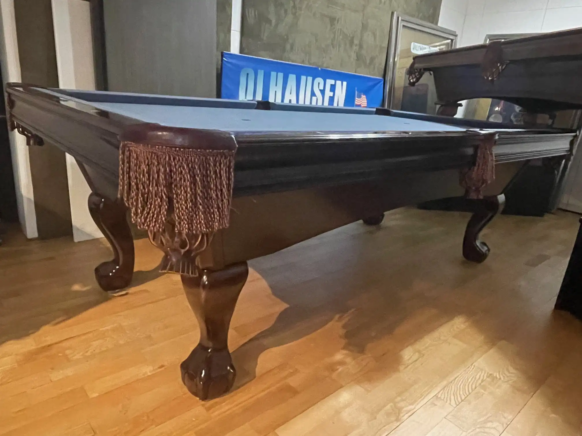 A traditional Brunswick Bradford cherry wood pool table with blue felt, carved ball and claw legs, and fringed leather pockets, seen from a low angle in a showroom