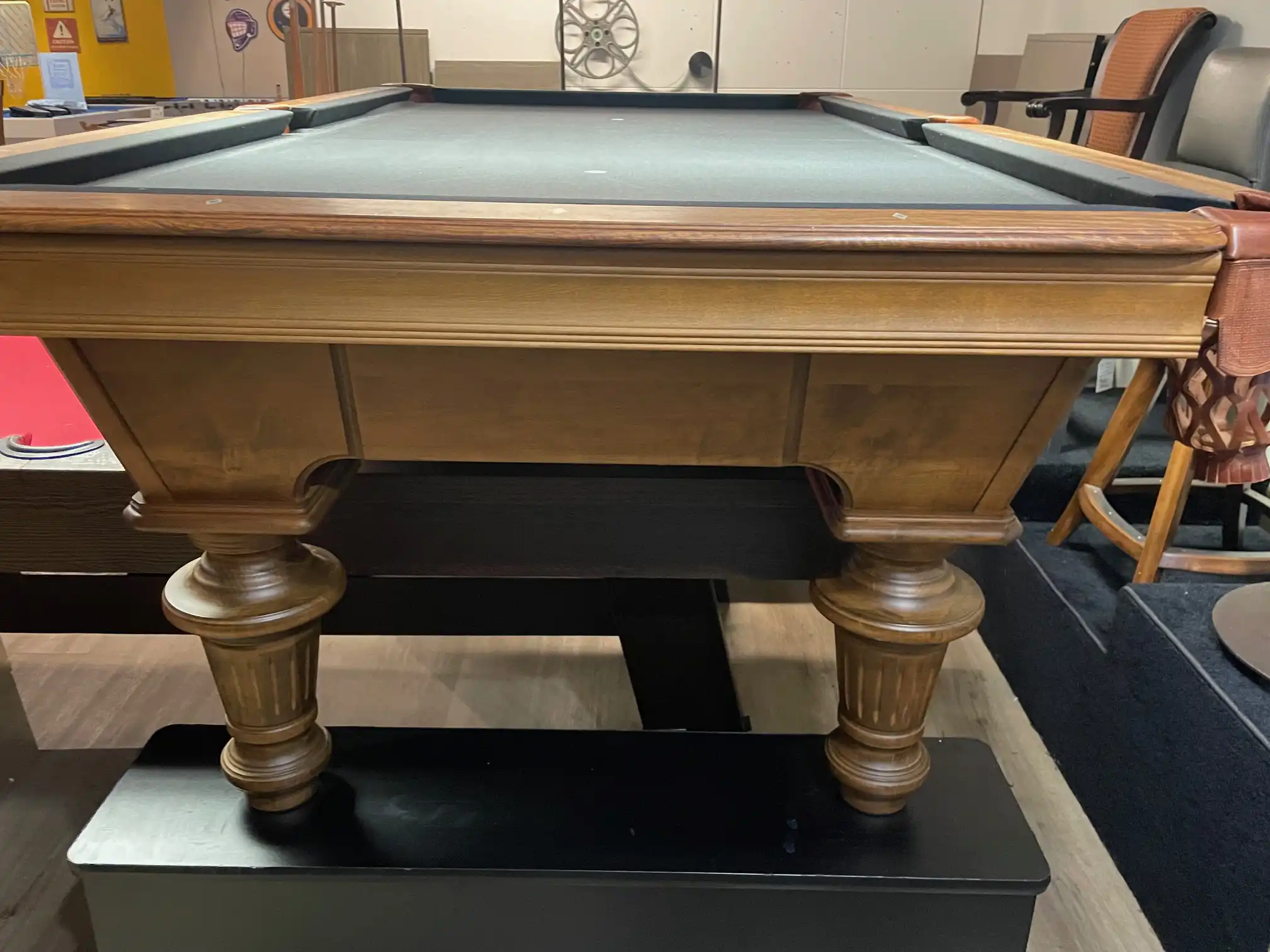 Olhausen Innsbruck pool table crafted from rich natural wood, featuring turned carved legs, brown leather pockets, and black felt cloth.