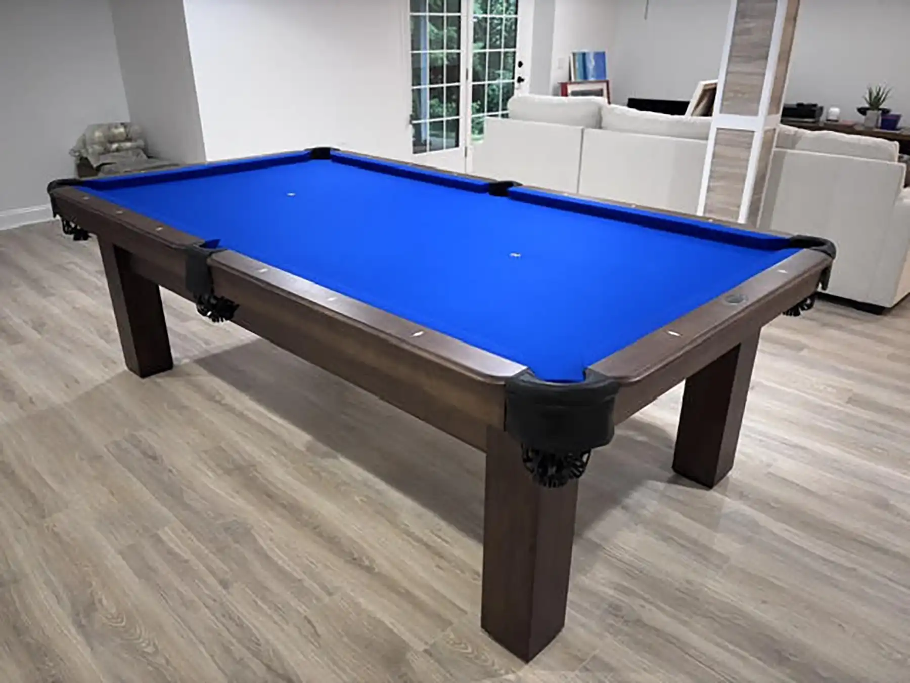 ontemporary wooden pool table with vibrant royal blue cloth placed on light hardwood floors in an open-concept finished basement and living area.