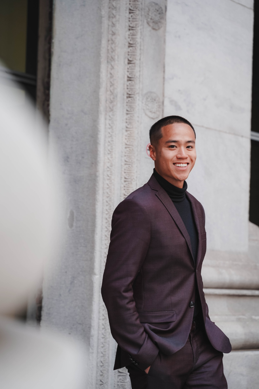 Smiling young Asian man wearing maroon suit walking outside