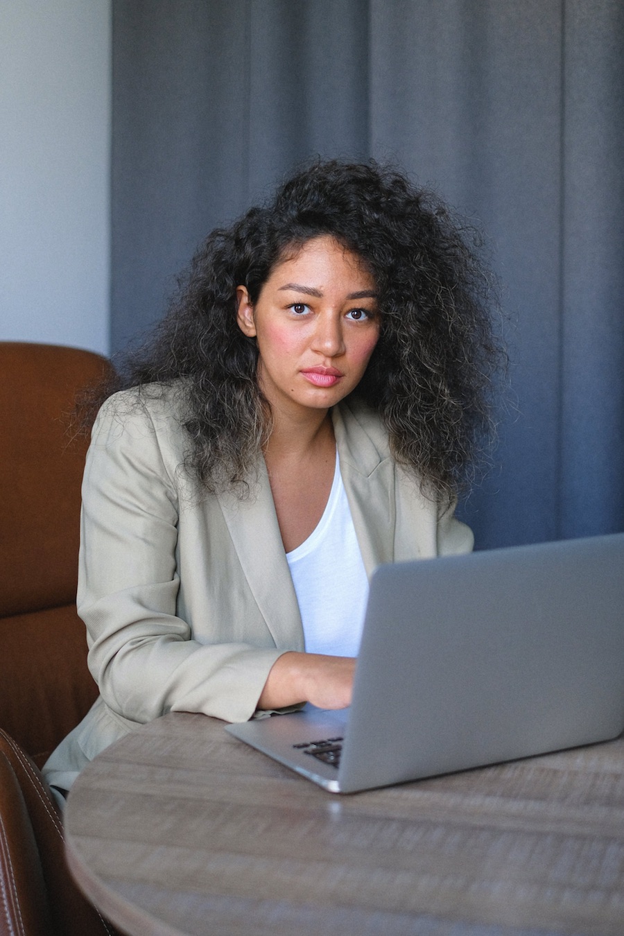 Woman with curly hair wearing business clothes sitting with laptop