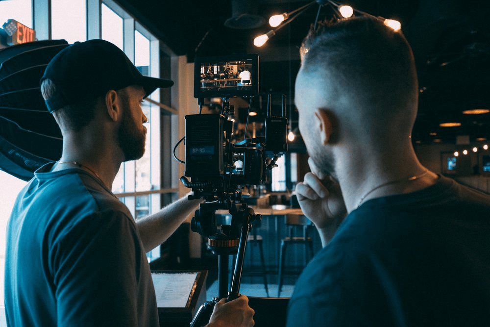 Two videographers reviewing footage on a camera monitor while filming inside a restaurant.