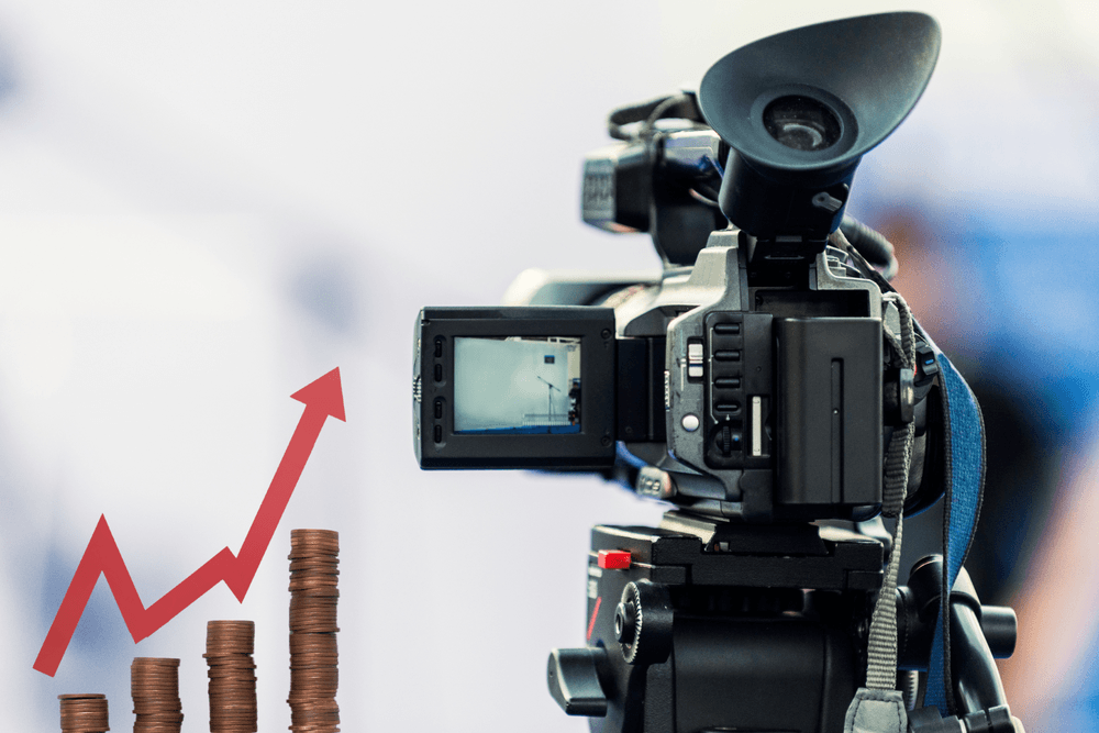 A professional video camera on a tripod alongside stacked coins and a red upward-trending growth chart, representing the return on investment and business growth driven by video marketing.