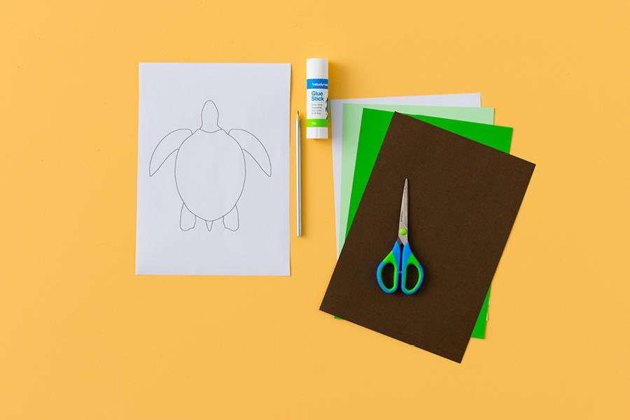 An assortment of products for making a paper turtle, arranged neatly on a yellow surface. Items include construction paper, a pencil, scissors and glue.