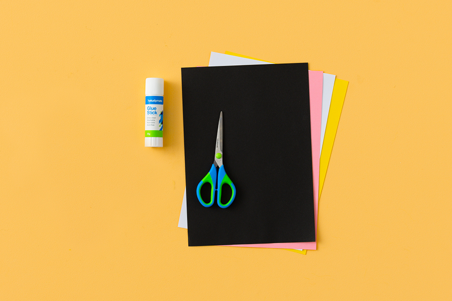 An assortment of products for making a paper yellow-tailed black cockatoo, arranged neatly on a yellow surface. Items include construction paper, scissors and glue.