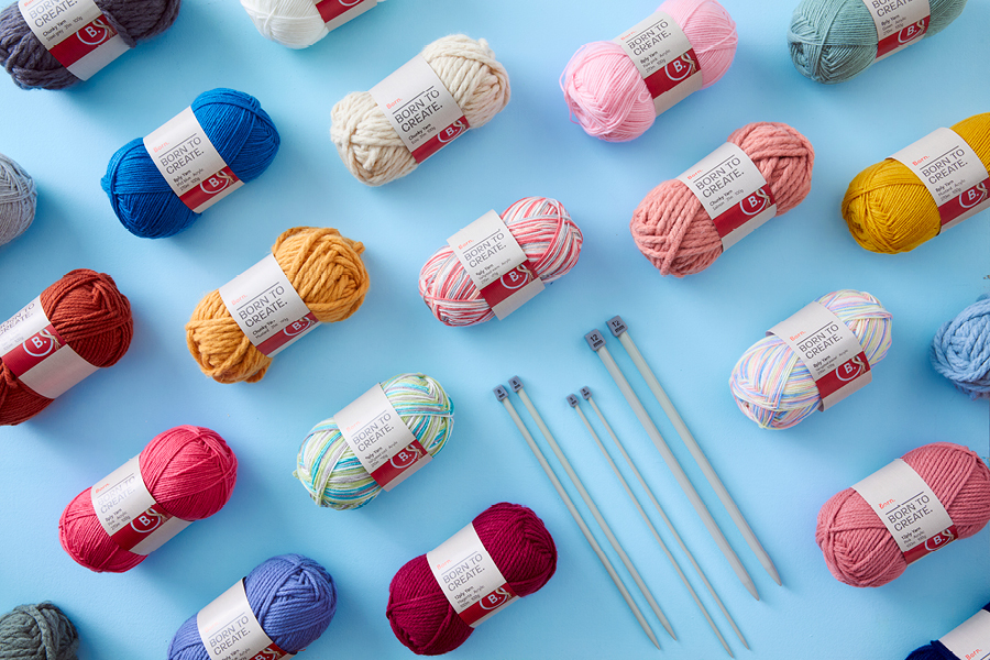 An assortment of Born knitting yarn and knitting needles, arranged in a neat pattern on a light blue background.