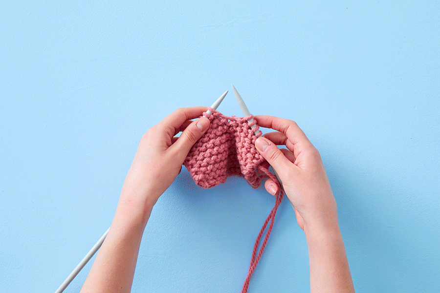 A series of images demonstrating how to do a knit stitch. They show an overhead view of two hands using two grey knitting needles and pink yarn.