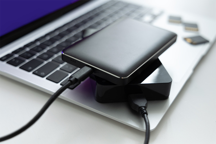 A close-up of two black data storage devices sitting on top of each other connected to a laptop via a USB cable.