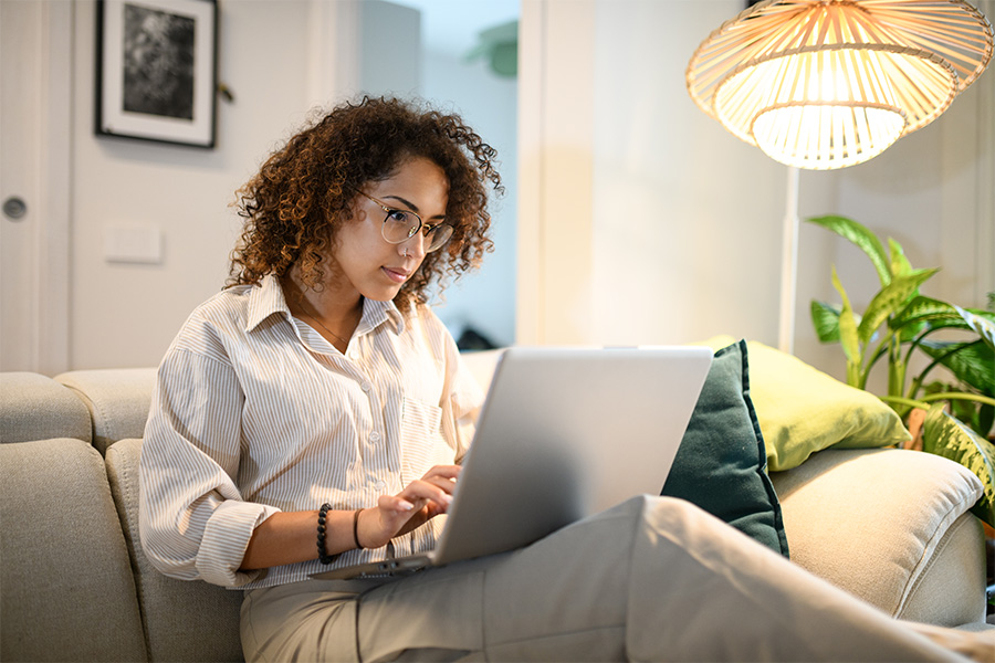 A person working on a laptop while sitting on a lounge in a cosy home environment.