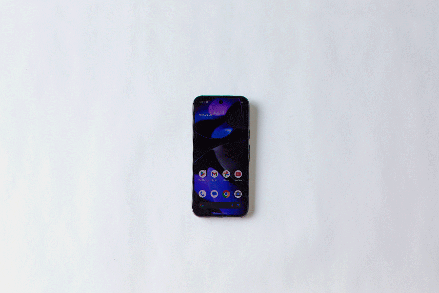 A series of images showing a hand reaching for a black Google Pixel 9 smartphone, using the touchscreen and turning it over, all shown against a white surface.