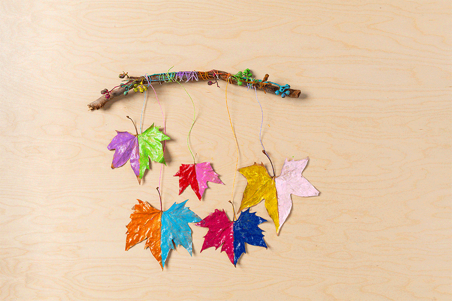 Two images showing supplies needed to craft a colourful leaf mobile, including leaves, a stick, paint and string, and the finished craft, both displayed on a wooden surface.
