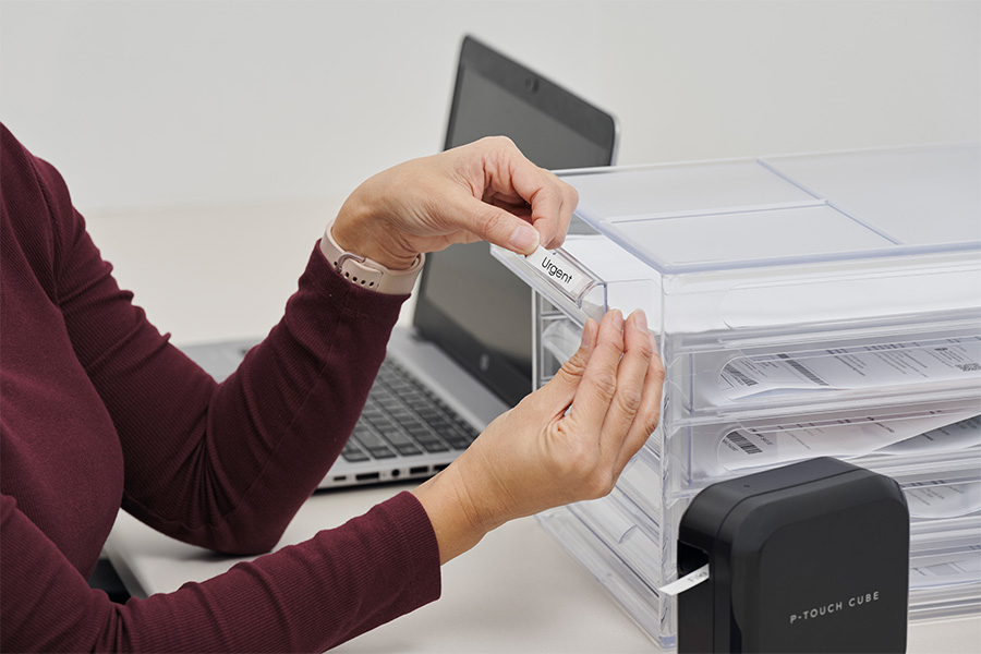 Pip Renfrew sitting at a desk labels document drawers with a printed label saying “Urgent”.
